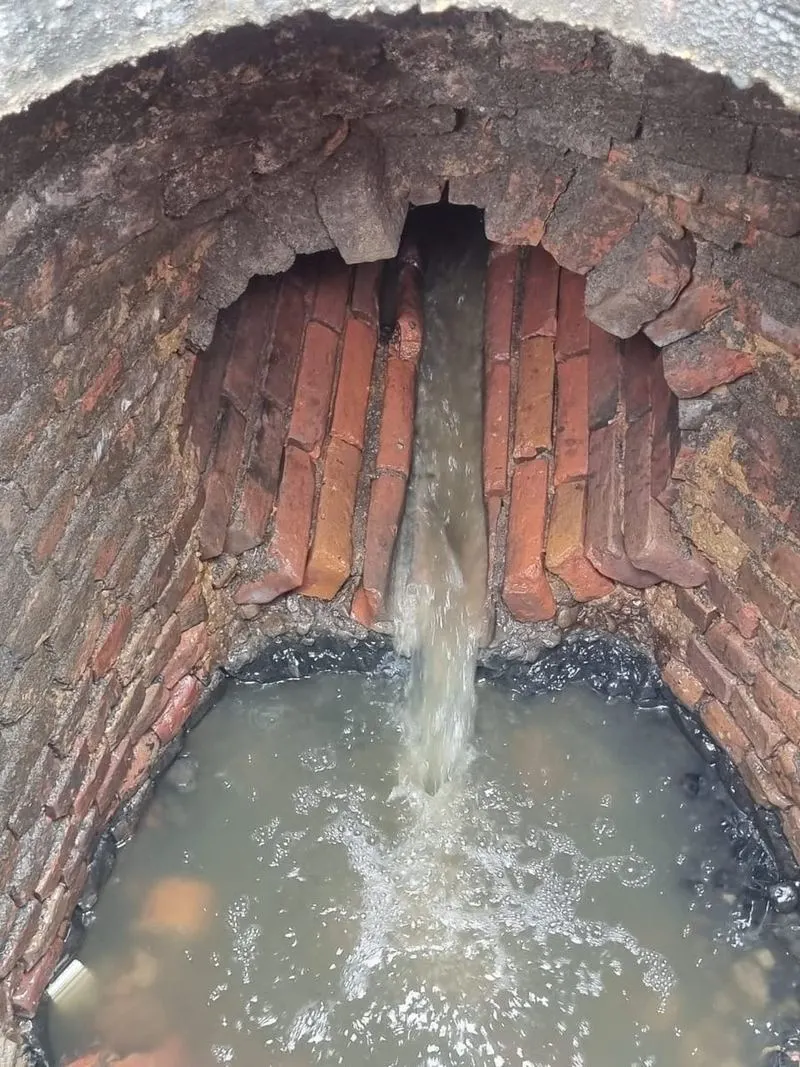 Water pouring from a pipe into an old brick chamber with a failing arch